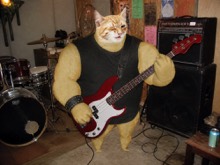 Swole Cat playing a red bass in a cluttered garage rehearsal space